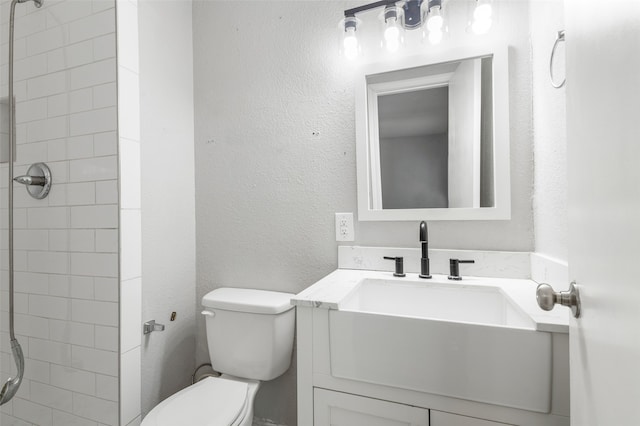 bathroom featuring a tile shower, vanity, and toilet