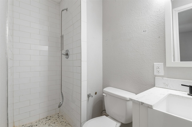 bathroom with a tile shower, vanity, and toilet