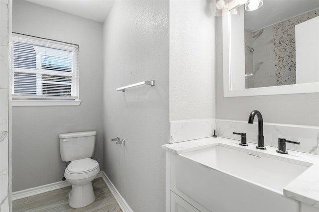 bathroom with a tile shower, wood-type flooring, vanity, and toilet