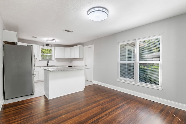 kitchen featuring a kitchen island, stainless steel fridge, white cabinetry, and dark hardwood / wood-style flooring