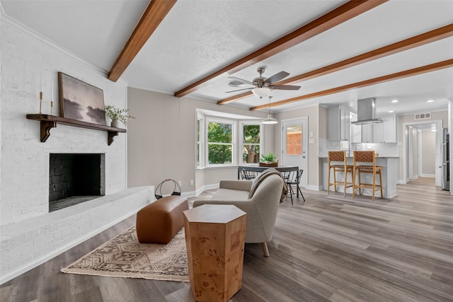 living room with a fireplace, ceiling fan, a textured ceiling, beam ceiling, and light hardwood / wood-style flooring