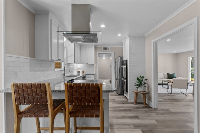 kitchen with light stone counters, island range hood, a kitchen breakfast bar, and white cabinets