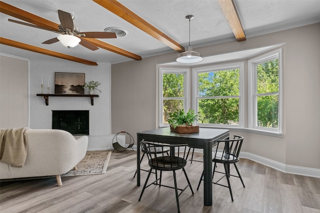 dining room featuring beamed ceiling, a fireplace, a textured ceiling, and hardwood / wood-style flooring