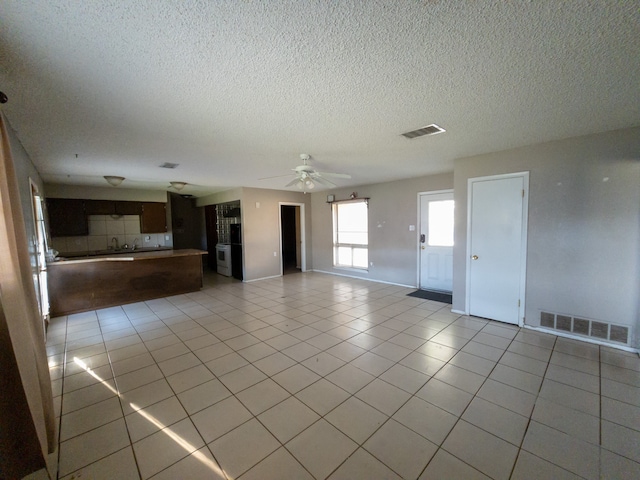 unfurnished living room with ceiling fan, a textured ceiling, and light tile patterned floors