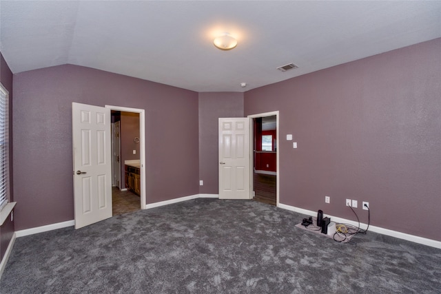 unfurnished bedroom featuring dark carpet, ensuite bath, and vaulted ceiling