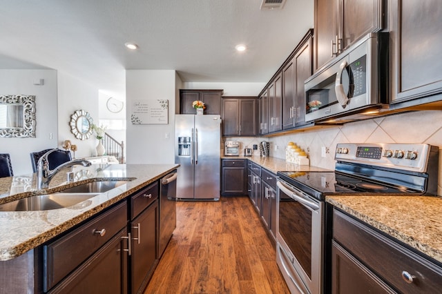 kitchen featuring sink, tasteful backsplash, dark wood-type flooring, stainless steel appliances, and light stone countertops