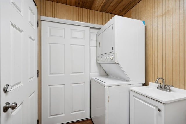 laundry area with sink, wood ceiling, stacked washer / dryer, and wooden walls