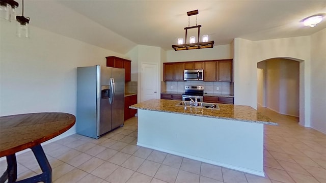 kitchen with an island with sink, light tile patterned floors, tasteful backsplash, decorative light fixtures, and appliances with stainless steel finishes