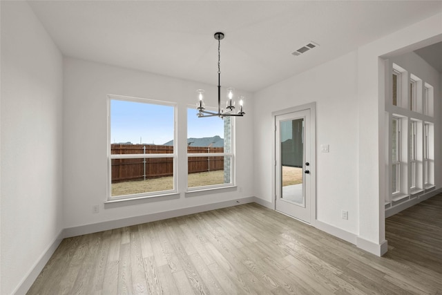 unfurnished dining area featuring a notable chandelier, baseboards, visible vents, and wood finished floors