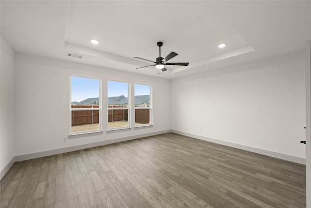 empty room featuring a mountain view, wood finished floors, visible vents, baseboards, and a raised ceiling