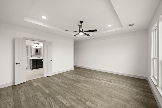 unfurnished bedroom with baseboards, visible vents, wood finished floors, a tray ceiling, and recessed lighting