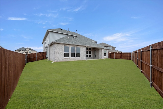 back of house featuring a yard, a fenced backyard, roof with shingles, and brick siding