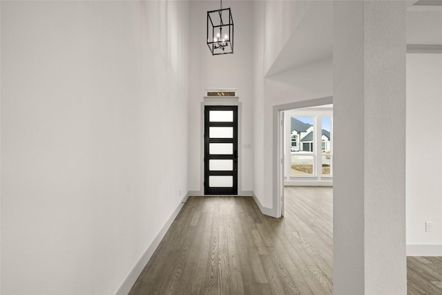 entryway featuring a towering ceiling, baseboards, a chandelier, and wood finished floors