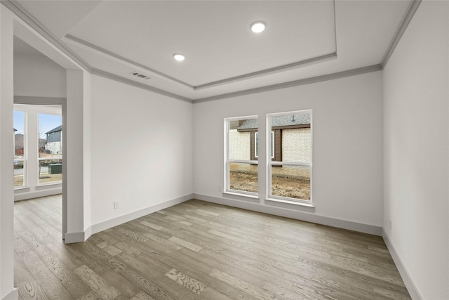 empty room featuring crown molding, a raised ceiling, visible vents, wood finished floors, and baseboards