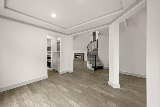 basement featuring baseboards, a glass covered fireplace, ornamental molding, wood finished floors, and stairs