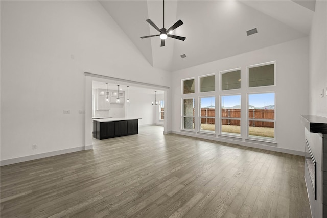 unfurnished living room with visible vents, wood finished floors, high vaulted ceiling, baseboards, and ceiling fan with notable chandelier