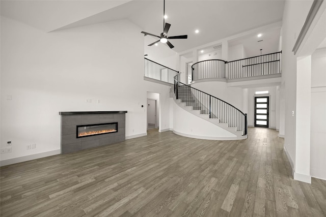 unfurnished living room featuring ceiling fan, wood finished floors, baseboards, stairs, and a tiled fireplace