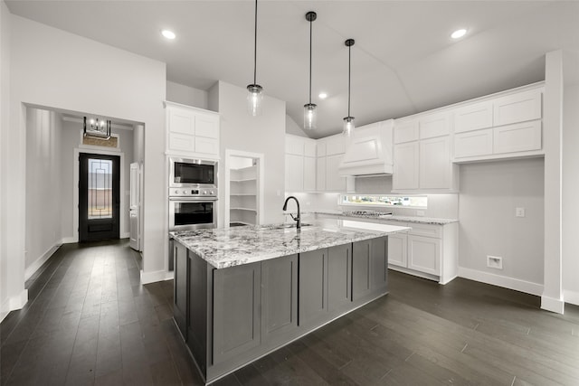 kitchen featuring light stone countertops, white cabinetry, appliances with stainless steel finishes, and a kitchen island with sink