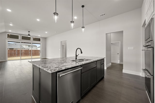 kitchen with appliances with stainless steel finishes, decorative light fixtures, sink, light stone countertops, and a center island with sink