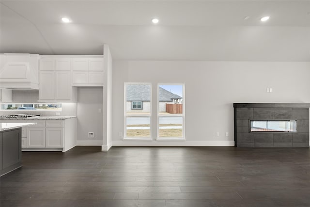 kitchen with custom exhaust hood, white cabinets, light stone counters, a fireplace, and dark hardwood / wood-style floors