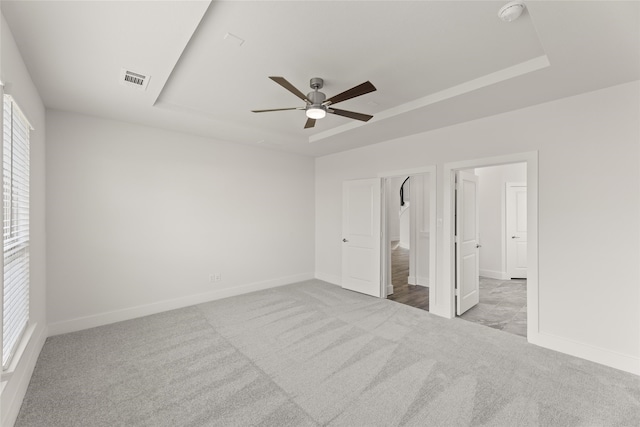 unfurnished bedroom with light carpet, a tray ceiling, and ceiling fan