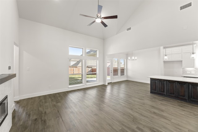 unfurnished living room with a tile fireplace, dark hardwood / wood-style flooring, high vaulted ceiling, and ceiling fan with notable chandelier