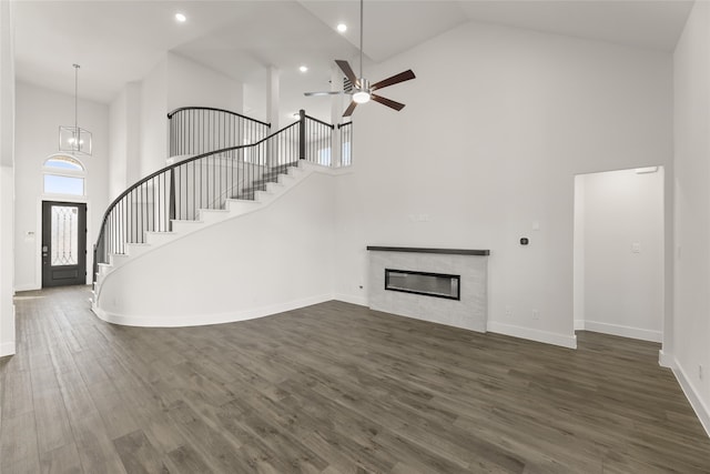 unfurnished living room featuring ceiling fan with notable chandelier, dark hardwood / wood-style flooring, high vaulted ceiling, and a tiled fireplace