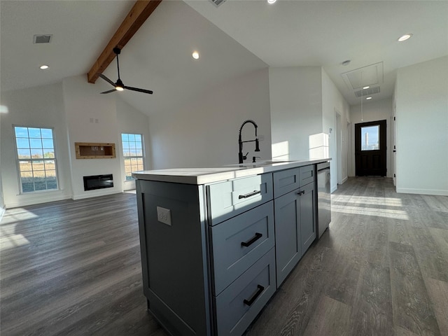 kitchen featuring dishwasher, dark wood-type flooring, ceiling fan, an island with sink, and beamed ceiling