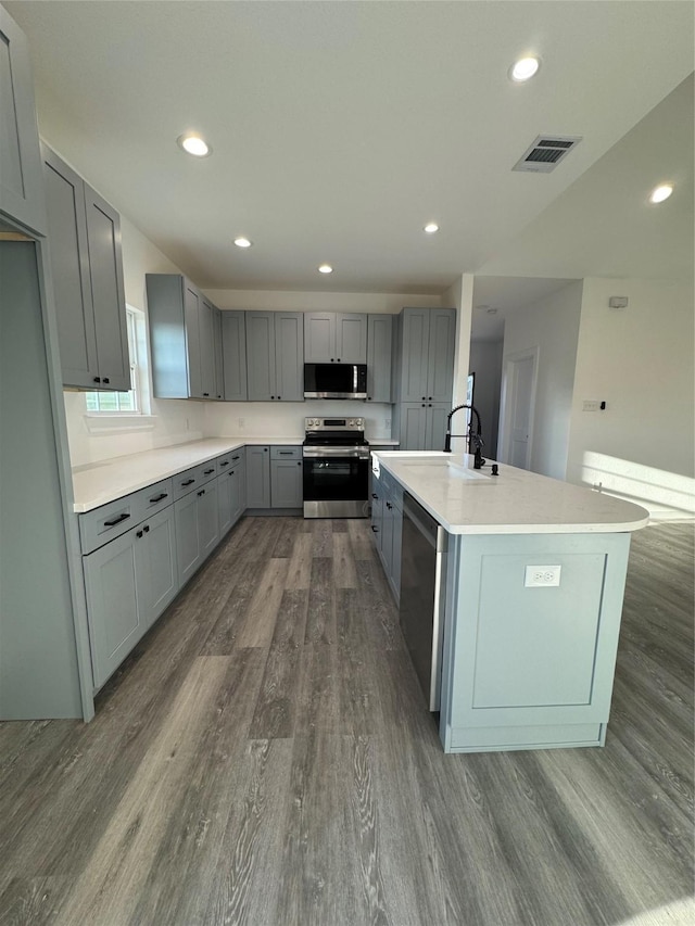 kitchen with appliances with stainless steel finishes, gray cabinetry, a kitchen island with sink, dark wood-type flooring, and sink