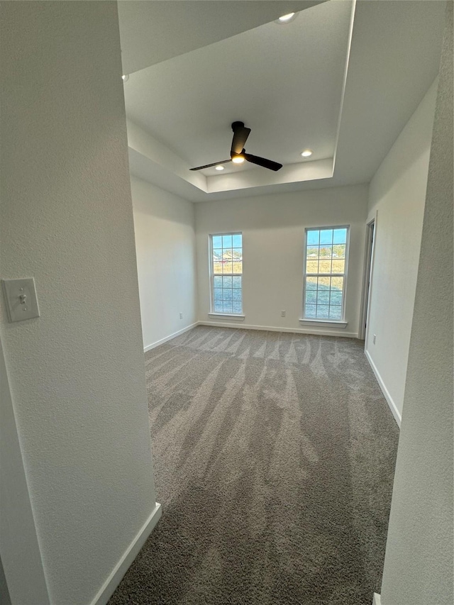 carpeted empty room featuring a raised ceiling and ceiling fan