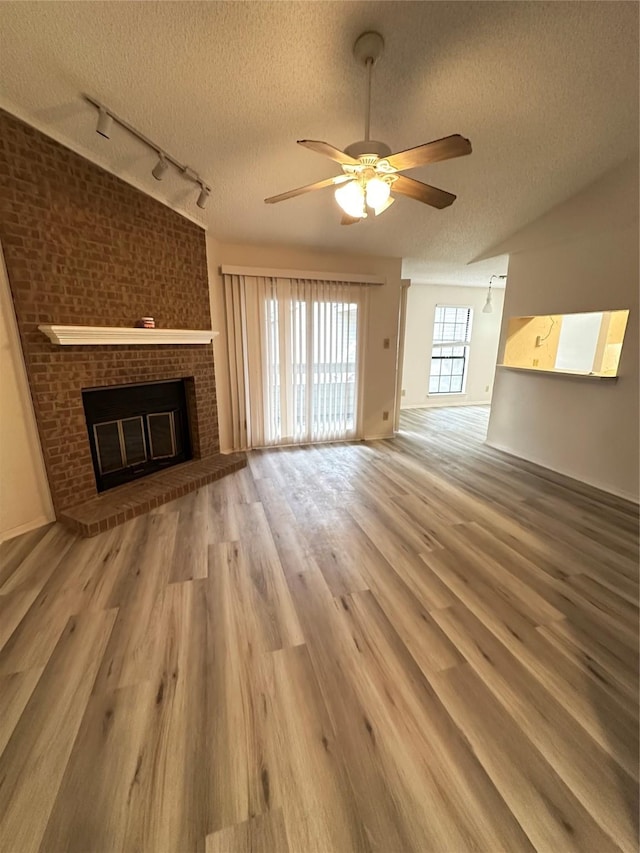 unfurnished living room with rail lighting, hardwood / wood-style flooring, ceiling fan, a fireplace, and a textured ceiling