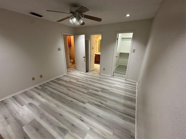 unfurnished bedroom with ensuite bath, ceiling fan, a spacious closet, a textured ceiling, and a closet