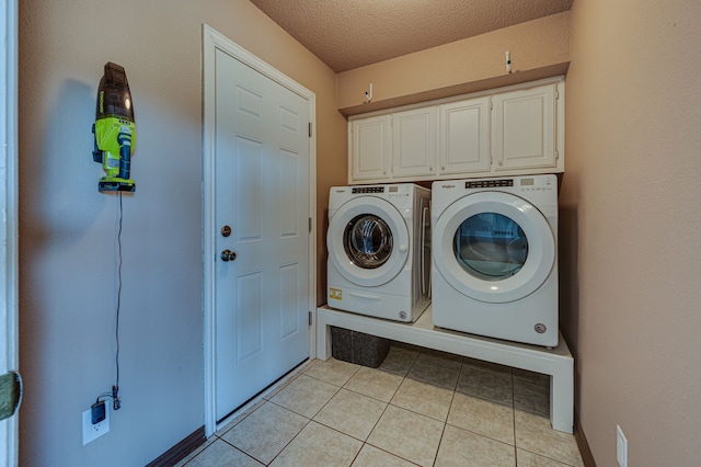 clothes washing area with cabinets, a textured ceiling, washer and dryer, and light tile patterned floors