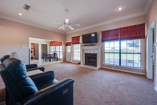 carpeted living room featuring washer / clothes dryer, a tiled fireplace, a textured ceiling, crown molding, and ceiling fan