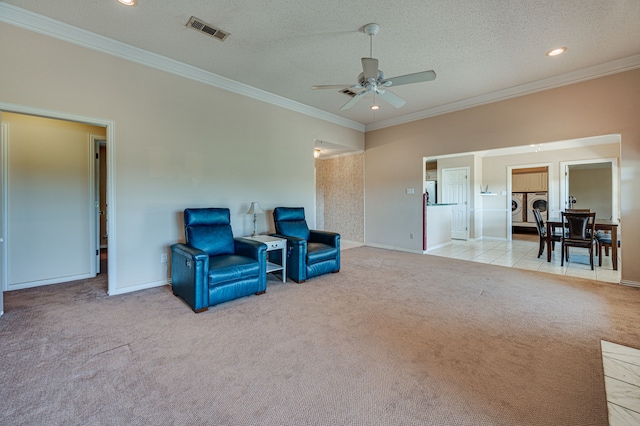 living area featuring a textured ceiling, crown molding, ceiling fan, light carpet, and washer and dryer