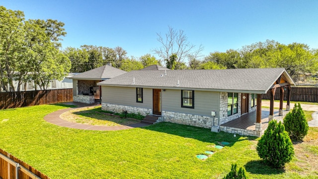 view of front facade featuring stone siding, a fenced backyard, a front lawn, and roof with shingles