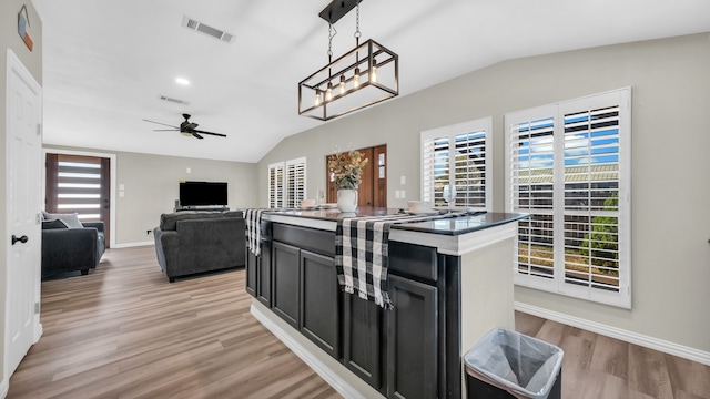 kitchen with light hardwood / wood-style floors, vaulted ceiling, ceiling fan with notable chandelier, a center island, and decorative light fixtures