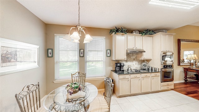 kitchen with tasteful backsplash, cream cabinets, hanging light fixtures, an inviting chandelier, and appliances with stainless steel finishes