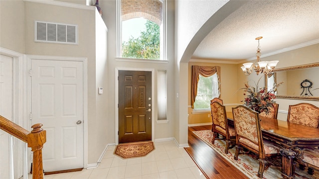 entryway with an inviting chandelier, light wood-type flooring, plenty of natural light, and ornamental molding