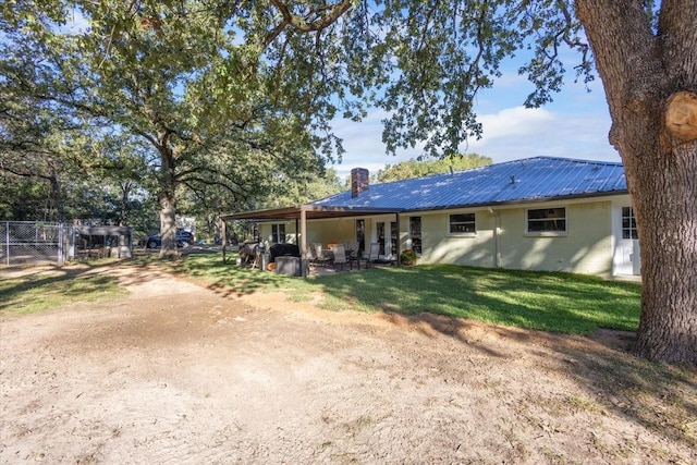 back of house featuring metal roof, a lawn, a chimney, fence, and stucco siding