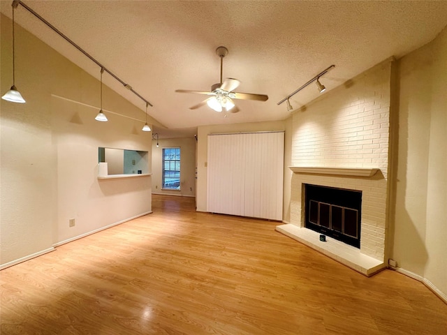 unfurnished living room featuring vaulted ceiling, a brick fireplace, a textured ceiling, ceiling fan, and hardwood / wood-style flooring