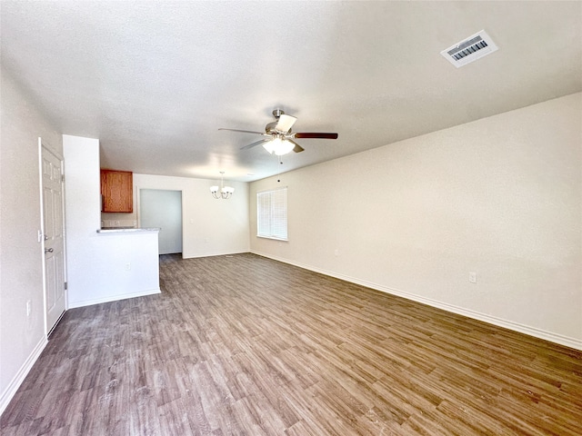 unfurnished living room featuring ceiling fan with notable chandelier, a textured ceiling, and dark hardwood / wood-style flooring