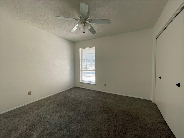 spare room featuring ceiling fan, dark carpet, and a textured ceiling