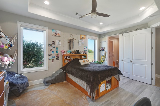 bedroom with a barn door, a raised ceiling, crown molding, ceiling fan, and light hardwood / wood-style flooring