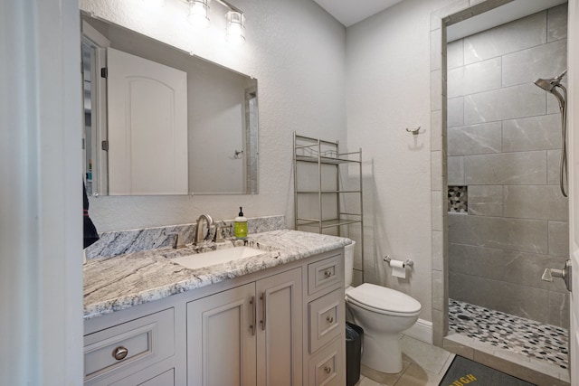 bathroom featuring tile patterned flooring, tiled shower, vanity, and toilet