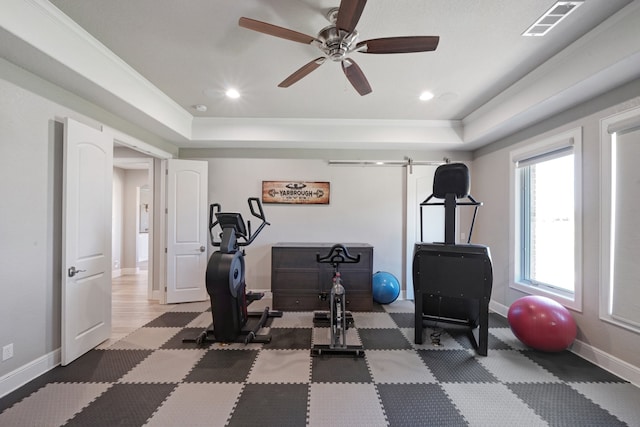 exercise room with a tray ceiling, ceiling fan, a barn door, and crown molding