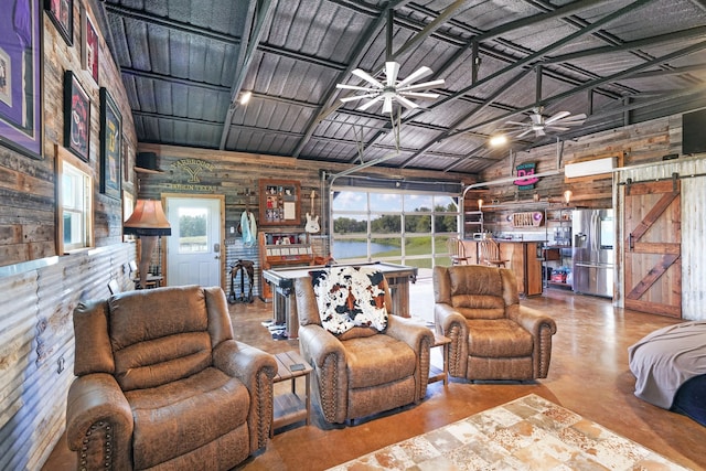 living room featuring high vaulted ceiling, wooden walls, ceiling fan, and a barn door