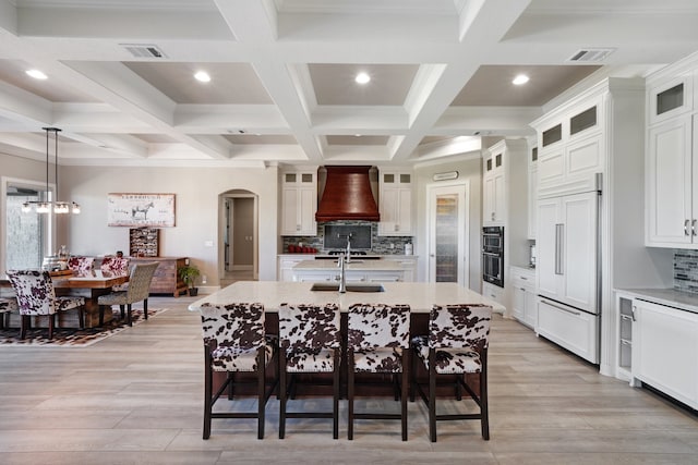 kitchen with paneled built in refrigerator, decorative backsplash, a center island with sink, and custom exhaust hood