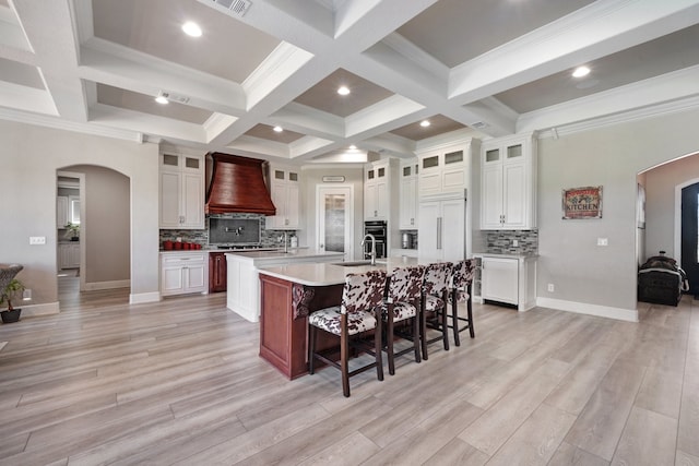 kitchen with a breakfast bar, tasteful backsplash, light hardwood / wood-style flooring, a spacious island, and premium range hood