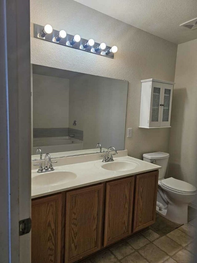 bathroom with a textured ceiling, vanity, toilet, and a tub